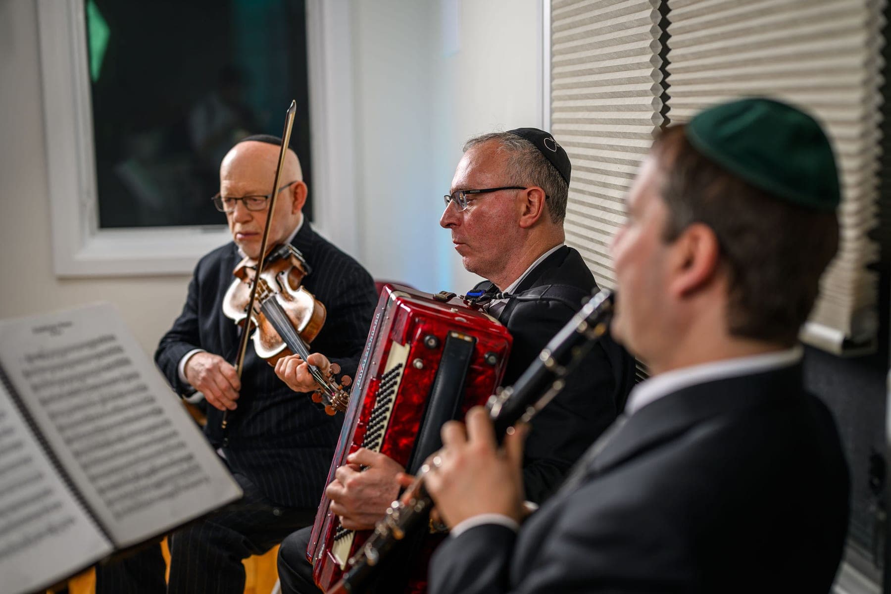 Three musicians playing violin, accordion and clarinet from stands