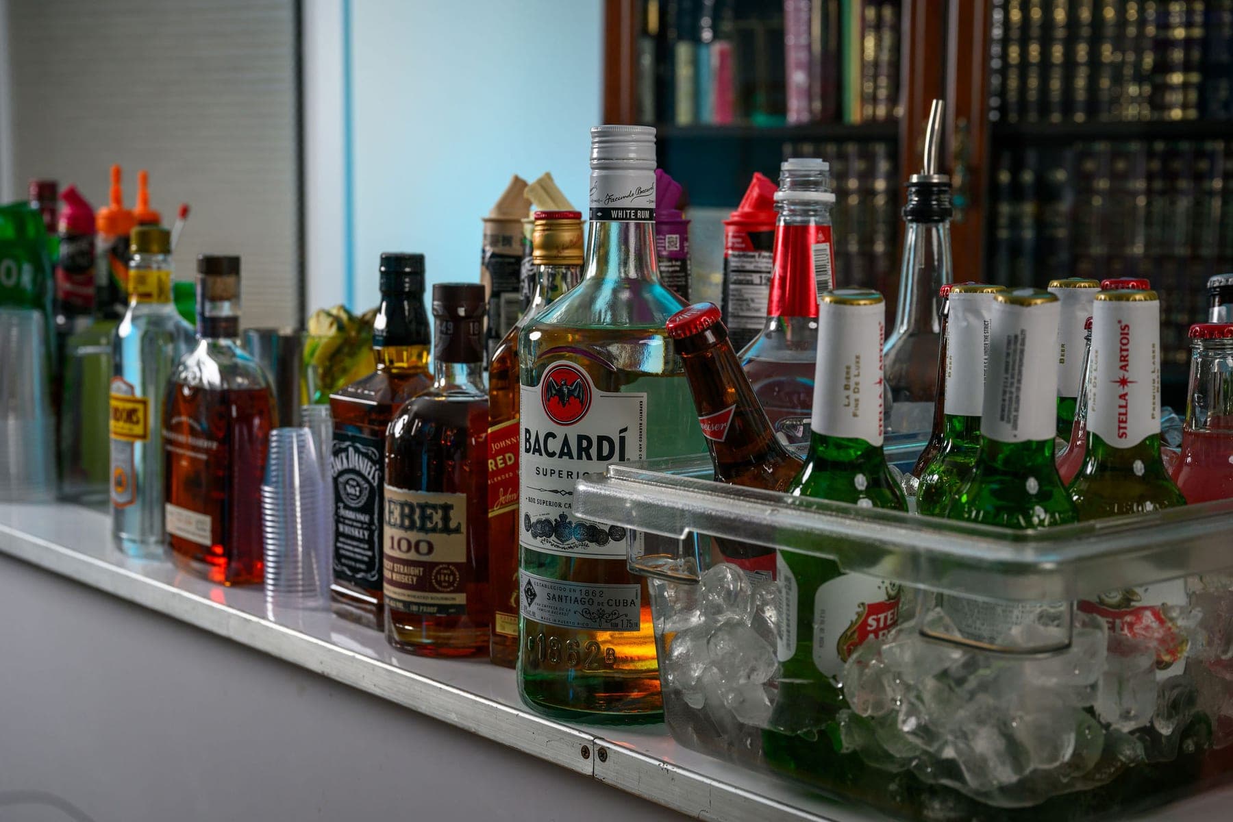 The bar laid along a shelf in front of bookcases, bottles and mixers on ice