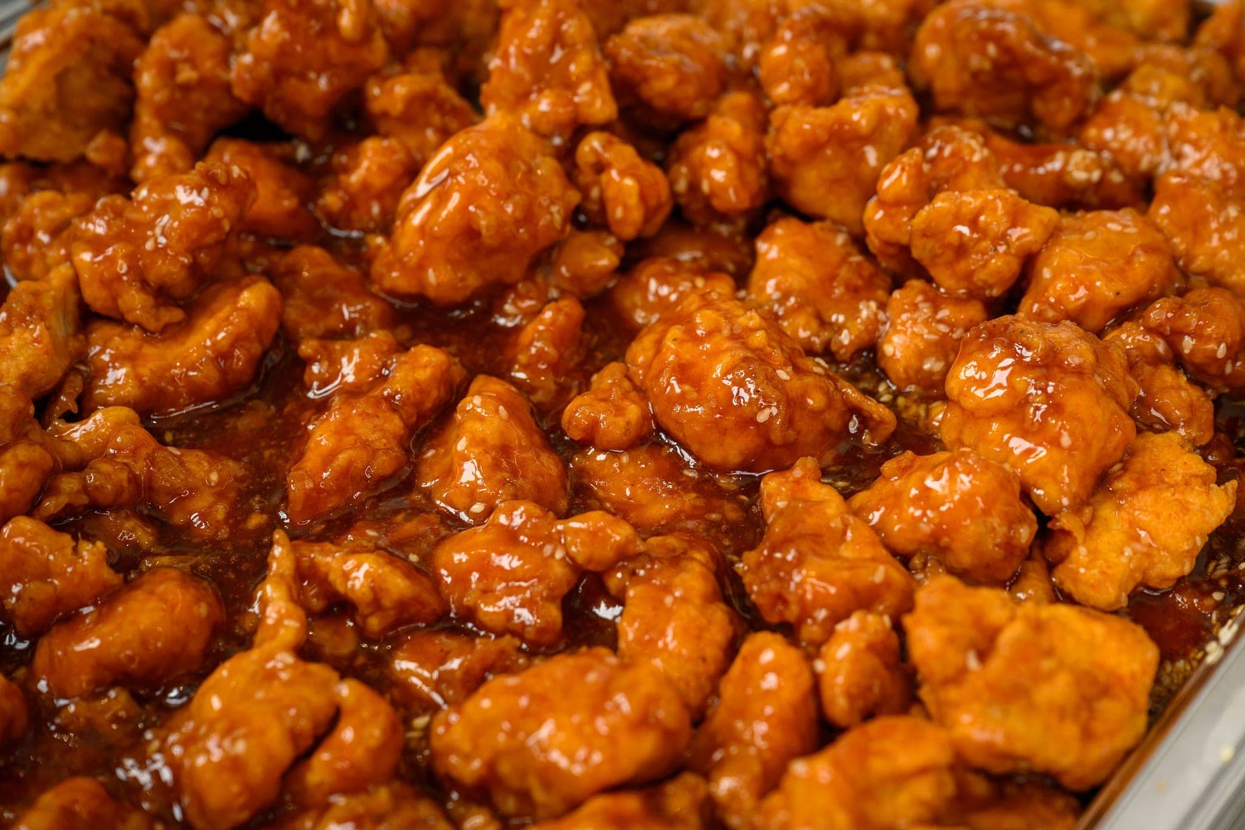 Sesame chicken in a glossy sauce, filling a tray