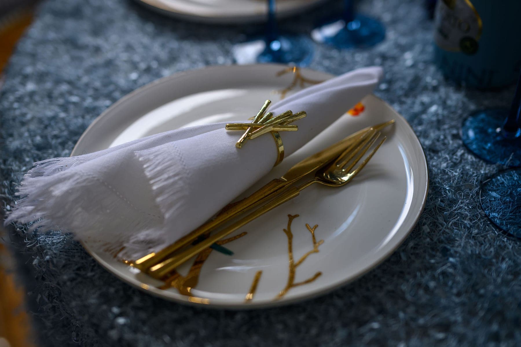 A place setting: white plate with a gold-tied napkin and gold cutlery on crushed ice