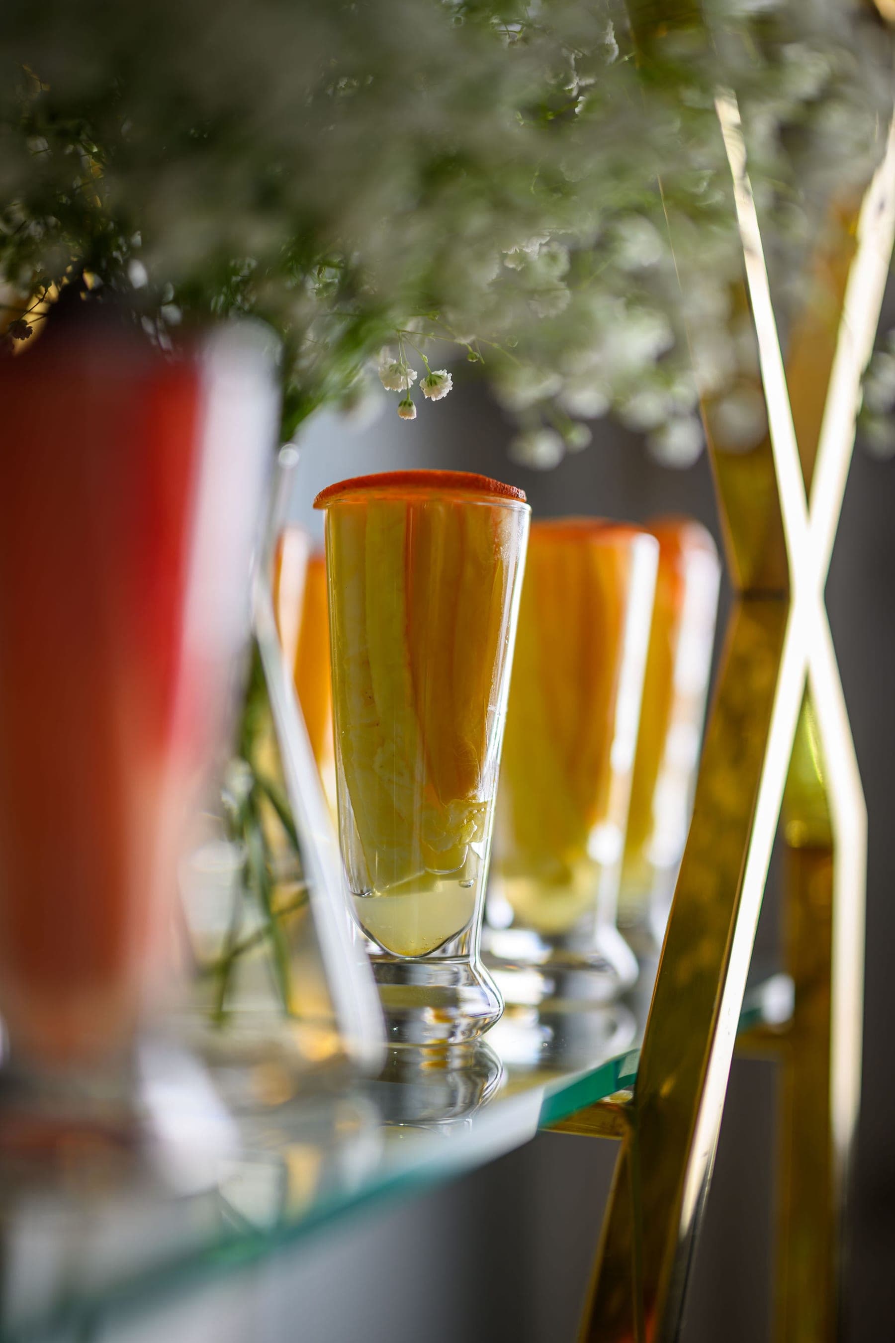 Tall glasses of a layered drink among gold stems and gypsophila